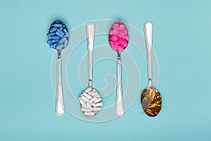 Table spoons filled with assortment of various colourful pills isolated on blue pastel coloured background. Antiobesity medication