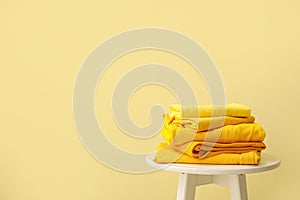 Table with stack of stylish clothes on color background