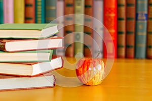 On the table are stacks of books and an apple.