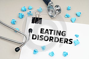 On the table is a stethoscope, a pen, blue crumpled pieces of paper and a sign with the inscription - EATNG DISORDERS