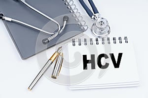On the table are a stethoscope, a pen and a notebook with the inscription - HCV