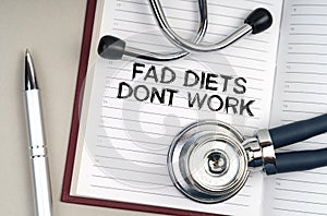 On the table is a stethoscope, a pen and a notebook in which it is written - Fad Diets Dont Work