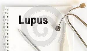 On the table are a stethoscope, a thermometer, a pen and a notebook with the inscription -Lupus