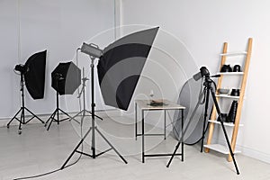 Table with stylish dinnerware in front of camera and professional lighting equipment indoors. Photo studio set