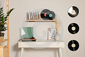 Table and stylish turntable near white wall decorated with vinyl records