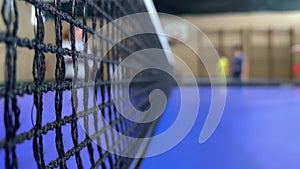 Table tennis net close-up with blurred players in the background