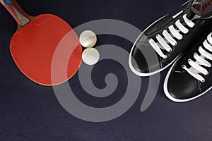 Table tennis racket, balls and black sneakers with white laces on a dark background