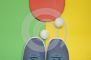 Table tennis racket, balls and sport sneakers on yellow green background