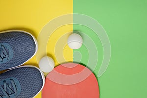 Table tennis racket, balls and sport sneakers on yellow green background