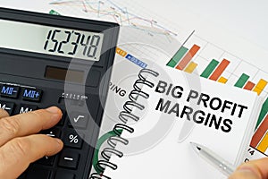 On the table there is a calculator, reports with graphs and a notepad with the inscription - Big Profit Margins