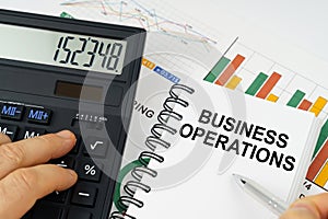 On the table there is a calculator, reports with graphs and a notepad with the inscription - Business Operations