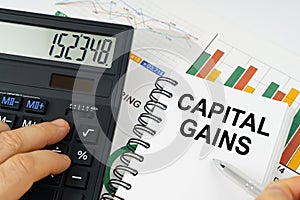 On the table there is a calculator, reports with graphs and a notepad with the inscription - Capital gains