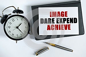 On the table there is a clock, a pen, a notebook and a card on which the text is written - IMAGE DARE EXPEND ACHIEVE