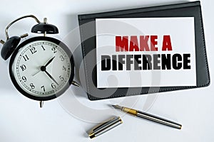 On the table there is a clock, a pen, a notebook and a card on which the text is written - MAKE A DIFFERENCE