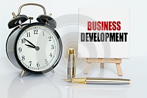 On the table there is a clock, a pen and a stand with a card on which the text is written BUSINESS DEVELOPMENT