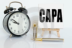 On the table there is a clock, a pen and a stand with a card on which the text is written CAPA. CORRECTIVE AND PREVENTIVE ACTION