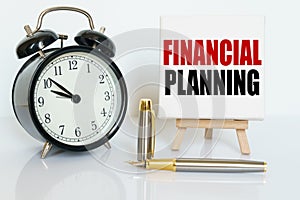 On the table there is a clock, a pen and a stand with a card on which the text is written - FINANCIAL PLANNING