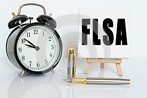 On the table there is a clock, a pen and a stand with a card on which the text is written FLSA. FAIR LABOR STANDARDS ACT