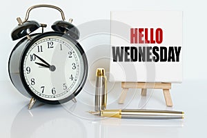 On the table there is a clock, a pen and a stand with a card on which the text is written - HELLO WEDNESDAY