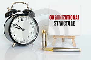 On the table there is a clock, a pen and a stand with a card on which the text is written - ORGANIZATIONAL STRUCTURE