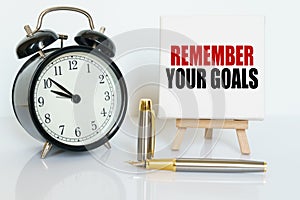 On the table there is a clock, a pen and a stand with a card on which the text is written - REMEMBER YOUR GOALS