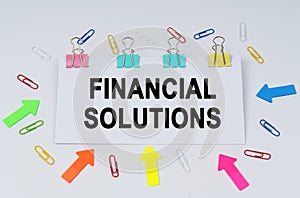 On the table there are paper clips and directional arrows, a sign that says - FINANCIAL SOLUTIONS