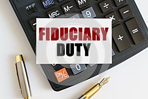 On the table there is a pen, a calculator and a business card on which the text is written - FIDUCIARY DUTY