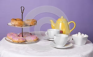 Table top filled with teacups, a teapot, sugar and donuts.