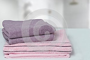 Table top on towels background. Closeup of a stack or pile of violet and pink soft terry bath towels at a bright table against