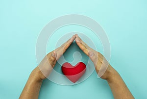 Table top view aerial image of hands protect of red heart on blue paper.Healthcare & medical or valentine background concept.