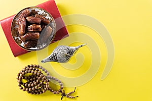 Table top view image of decoration Ramadan Kareem,  dates fruit, aladdin lamp and rosary beads on yellow  background. Flat lay