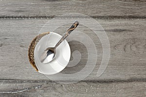 Table top view on small empty porcelain bowl with silver decorated spoon, placed on gray wood desk.