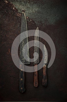 Table top view of three rustic knives on old rusty metallic background