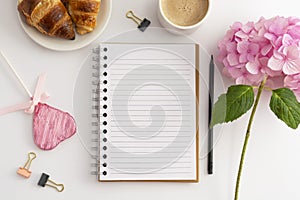 Table top of work space, feminine background. Cup of coffee with pink hydrangea and notebooks.