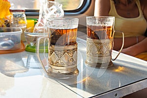 On the table in the train compartment are glasses with tea in metal cup holders