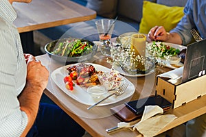 At the table, two men eat dinner, eat a steak, with a salad on a white plate, with a fork and knife in their hands.