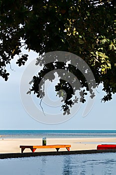 table under shade and tree on the beach with ocean and pool in a scene on evening sunlight