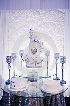 Table with a wedding cake, candles and flowers. Photo-wall, wedding decoration space or place from white and silver