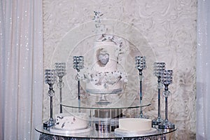 Table with a wedding cake, candles and flowers. Photo-wall, wedding decoration space or place from white and silver