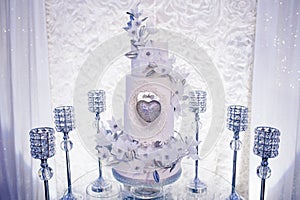 Table with a wedding cake, candles and flowers. Photo-wall, wedding decoration space or place from white and silver