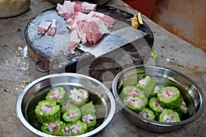 Table where the food is prepared, chopping board with slices of pork and two bowls with filled bitter gourd.