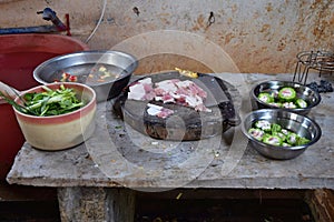 Table where the food is prepared, chopping board with slices of pork and two bowls with filled bitter gourd.