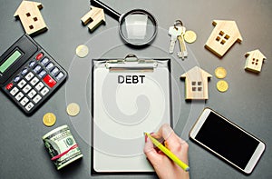 Table with wooden houses, calculator, coins, magnifying glass with the word Debt. The concept of debt for housing. Mortgage.