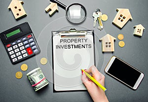 Table with wooden houses, calculator, coins, magnifying glass with the word Property investments. Attracting investment in your