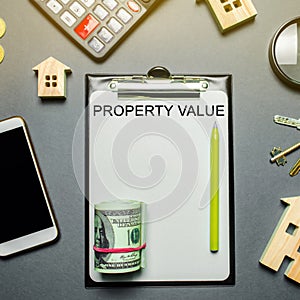 Table with wooden houses, calculator, coins, magnifying glass with the word Property value. The contract for real estate appraisal photo