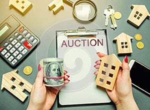 Table with the word Auction. The women auctioneer is holding money in the hands of dollars and a wooden house. Purchase and public