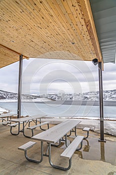 Tables and benches inside a pavilion overlooking an icy lake with snowy shore