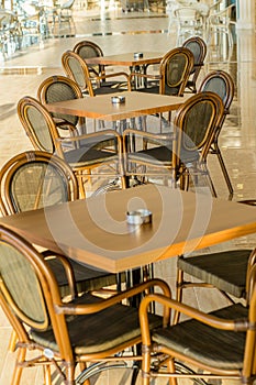 Tables and chairs in the cafe on the terrace. There are no visitors. In the background, you can see the pool. On standing ashtrays