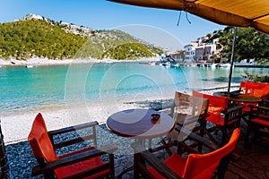 Tables with chairs of cozy Greek tavern restaurant in front of the beach in Assos village on Kefalonia island in Greece