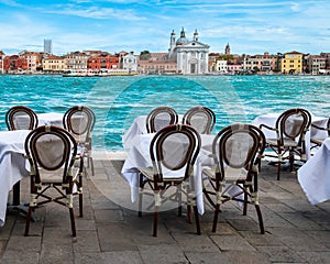 Tables and chairs outdoor a restaurant with canal view in Venice, Italy.